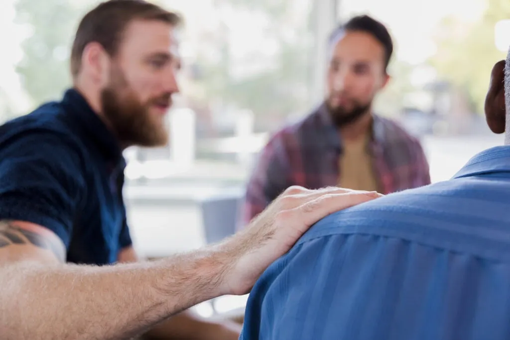 porchlight-recovery-sober-community Mid adult man comforts friend during therapy sesion