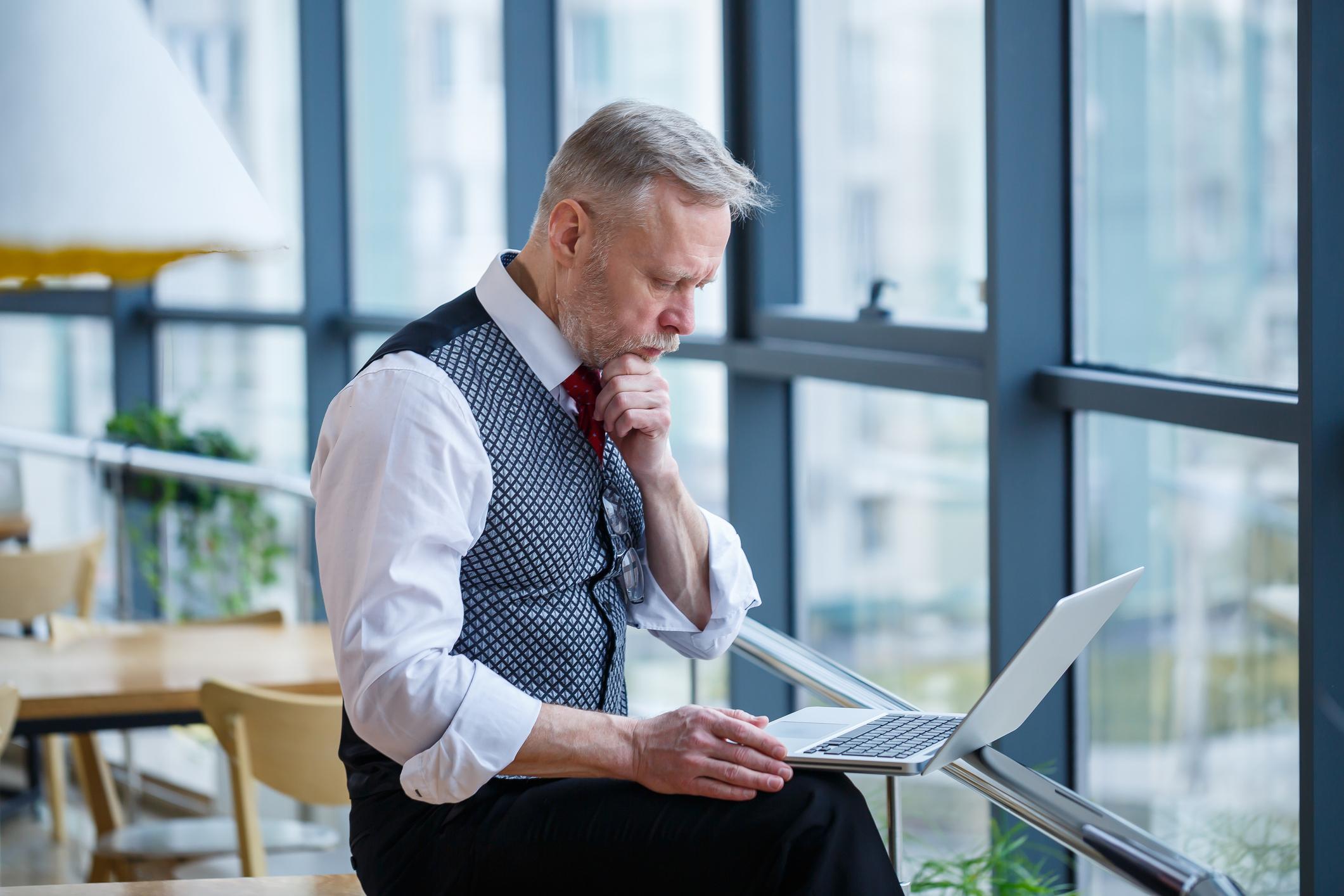 Mature professional working at a laptop, reflecting on career opportunities and a new chapter.