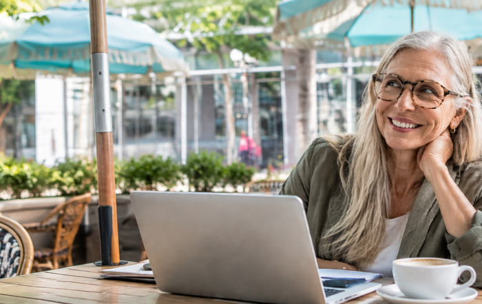 Smiling silver-haired professional woman working on a laptop at an outdoor café, representing hope and career rebuilding after addiction.